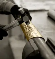 Detail of the handcrafted process in the creation of Castro Lighting's luxury lamps, with a hand working on a metal piece using a hammer.
